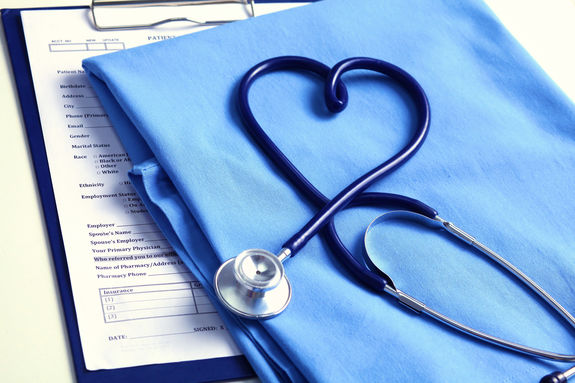 Medical stethoscope twisted in heart shape lying on patient medical history list and blue doctor uniform closeup